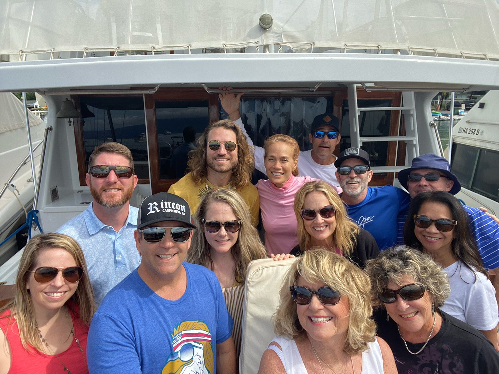 A group in sunglasses smiling for a selfie on the deck of a boat in a Maui harbor.
